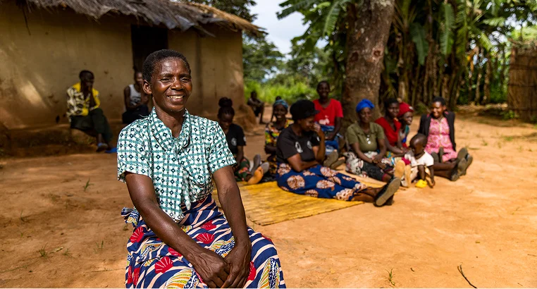 Smiling woman seated outdoors with a group of people in a rural African community