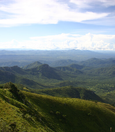 A panoramic view of lush green hills and mountains beneath a partly cloudy blue sky.