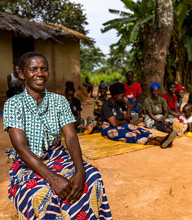 Smiling woman seated outdoors with a group of people in a rural African community